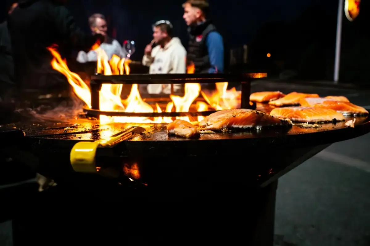 Saumon grillé sur la plancha du brasero, invités en arrière-plan